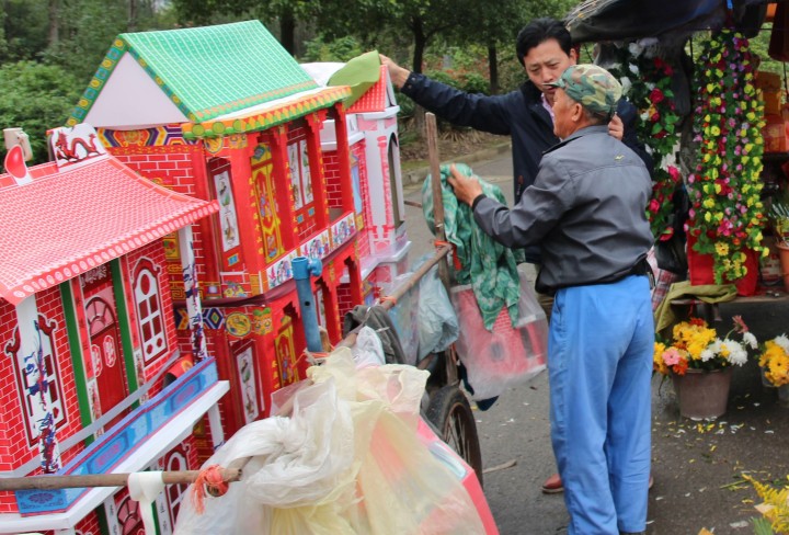 Zwei Männer vor menschengroßen Papierhäusern am Friedhof von Nanking in China