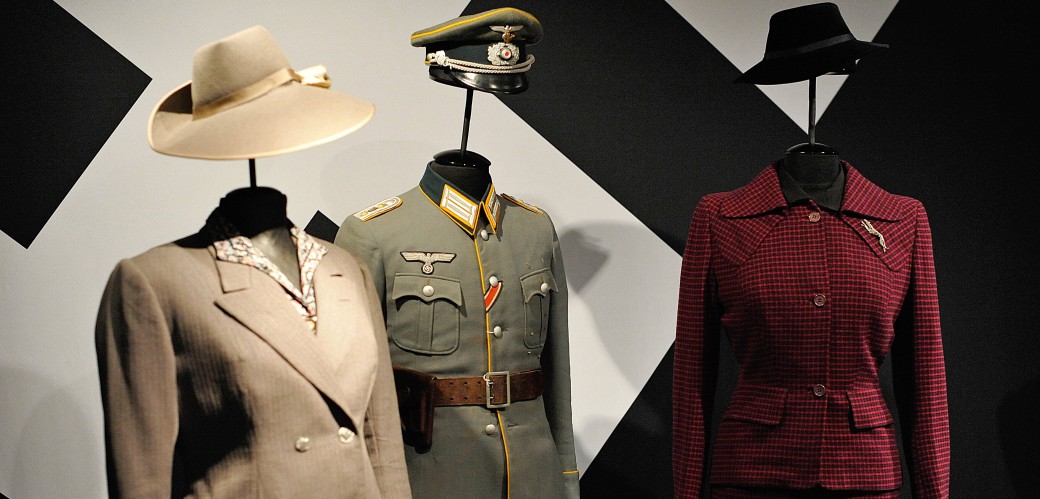Zwei Kostüme für Damen und eine Uniform an Figurinen in der Ausstellung