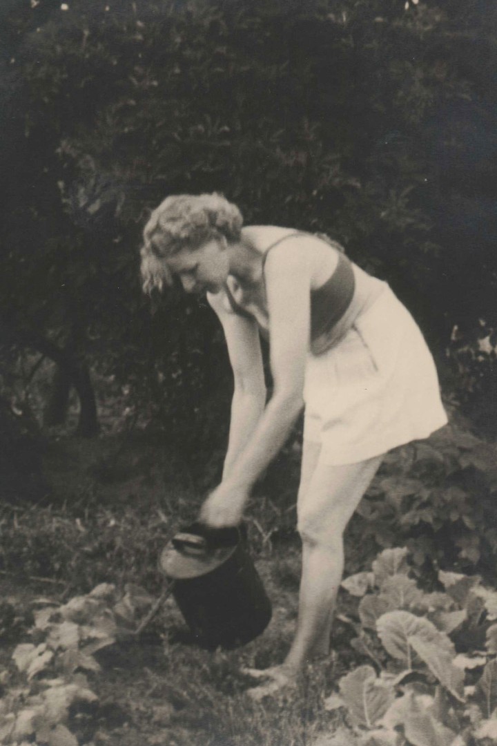 Historisches Schwarzweiß-Foto von einem sommerliche gekleideten Mädchen, das Gemüse gießt