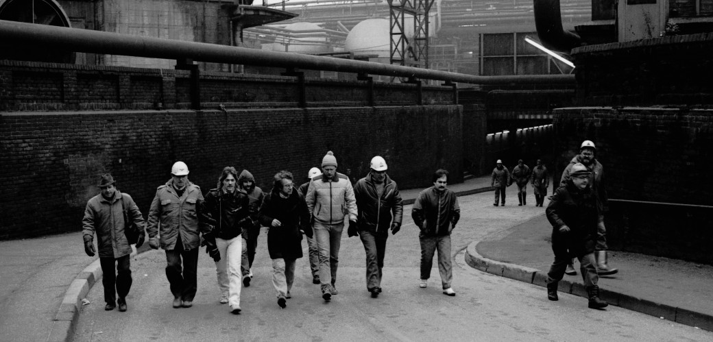Historisches Schwarzweißfoto von Männern, die in einer Industrieanlage in einer Reihe laufen