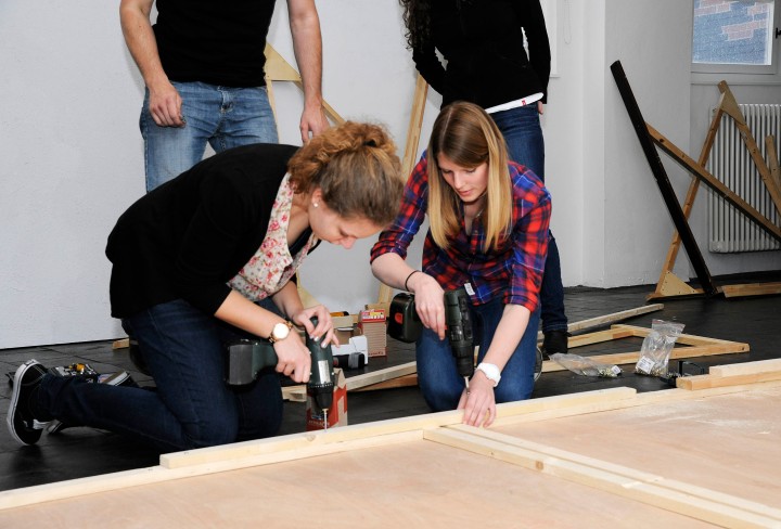 Schülerinnen bearbeiten ein Holzstück zum Bau einer Arbeiterküche