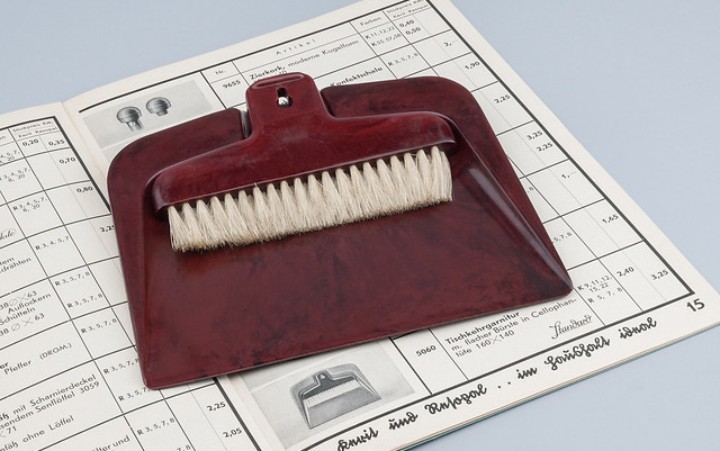 A hand brush and dustpan lie on a newspaper.