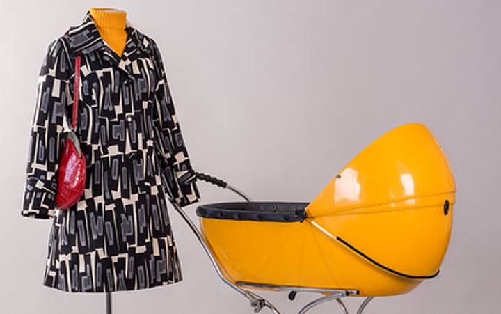 A dress form is dressed in a patterned coat and appears to be pushing a yellow stroller.