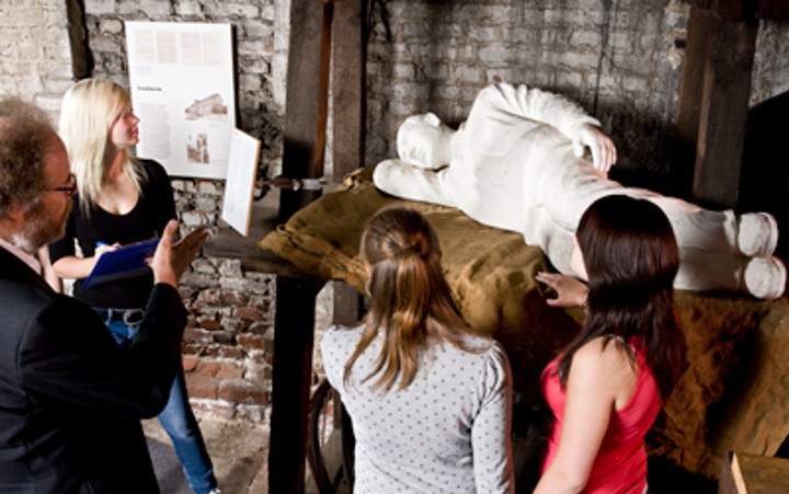 Jugendgruppe bekommt von Museumsmitarbeiter eine weiße, liegende Figur gezeigt