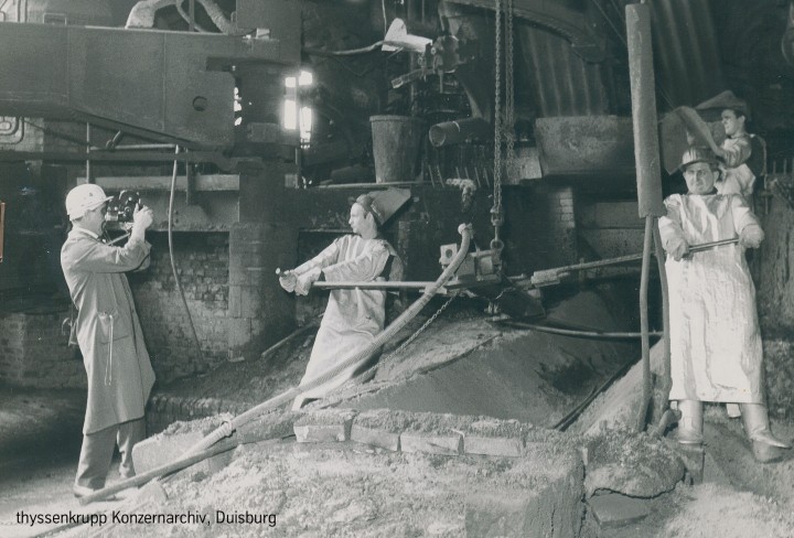 Schwarzweiss-Foto zeigt Männer, die am Hochofen arbeiten