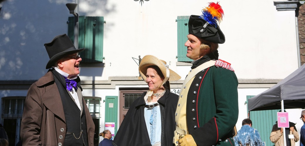 Drei Menschen mit historischen Kostümen unterhalten sich, darunter Hüttendirektor Gottlob Jacobi