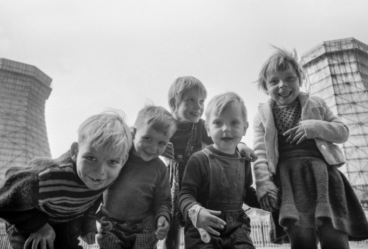 Schwarz/Weiß Aufnahme von fünf Kindern vor einer Industrieanlage die in die Kamera lachen