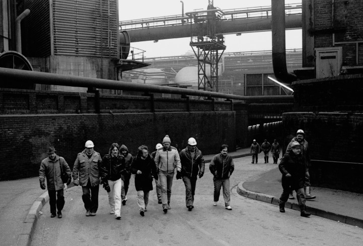 Schwarzweiß-Foto einer Gruppe Männer, die durch eine Industrieanlage laufen