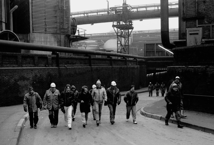 Historisches Schwarzweiß-Foto von Arbeitern, die gemeinsam über ein Fabrikgelände laufen