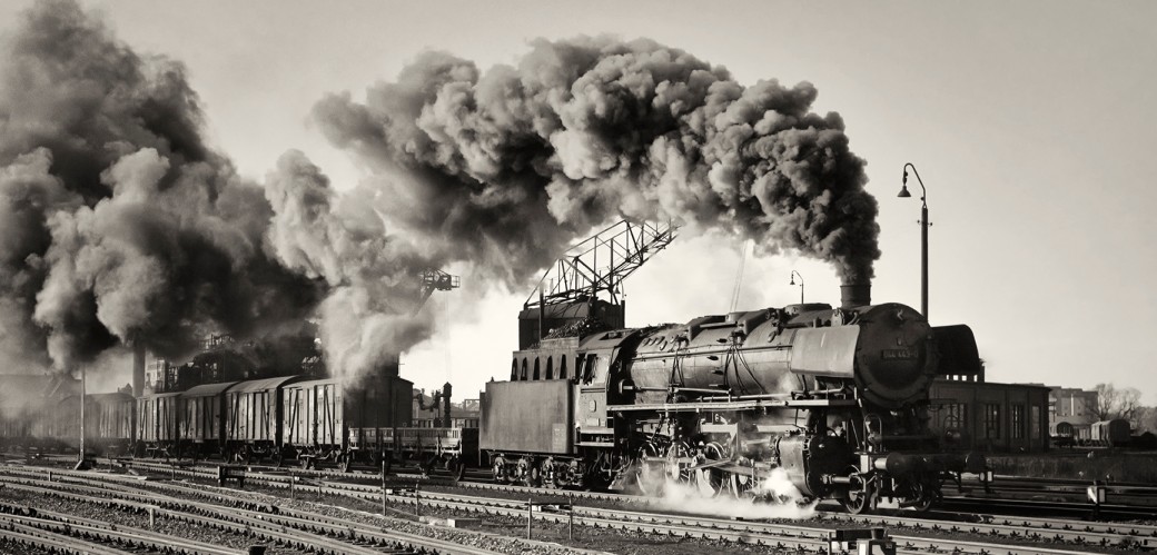 Schwarz-Weiß-Fotografie: Blick auf eine historische Eisenbahn, aus der viel Dampf steigt