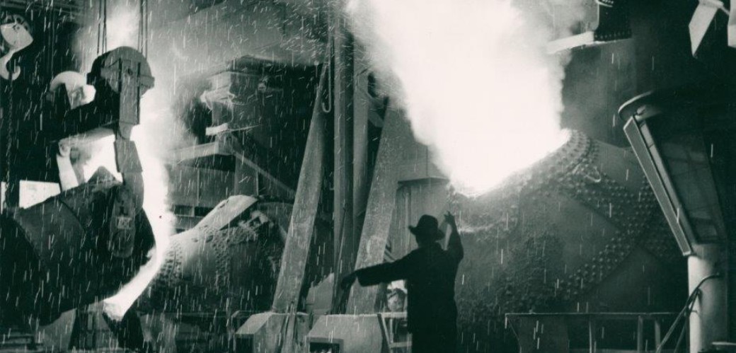 Schwarz-weiß-Foto eines Mannes in einem Werk, im Hintergrund sprühen Funken