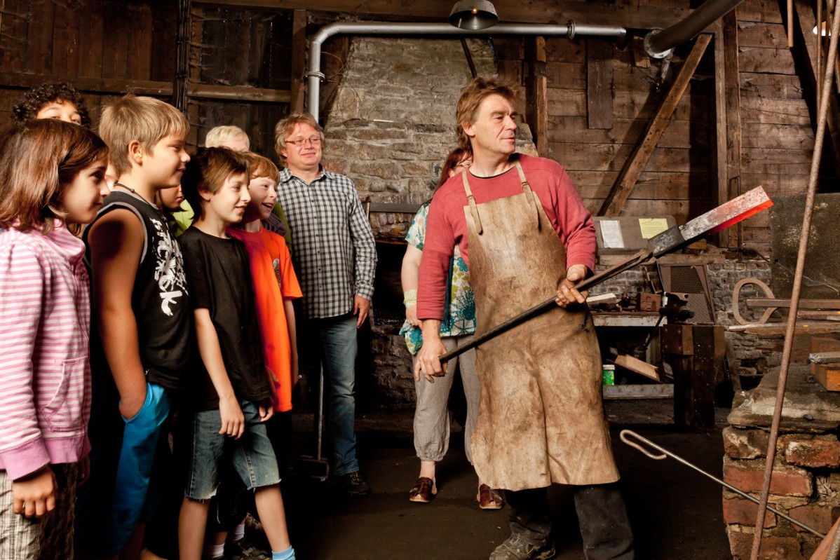 Museum blacksmith shows a group of children at the furnace a red-hot workpiece.