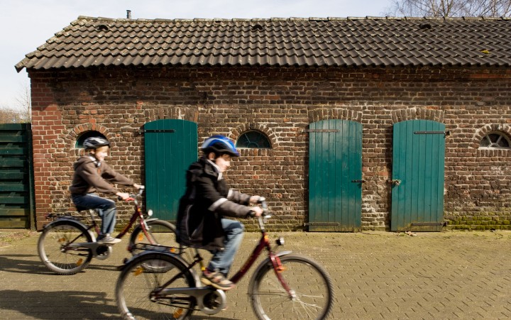 Two boys quickly cycle past historic buildings on bicycles