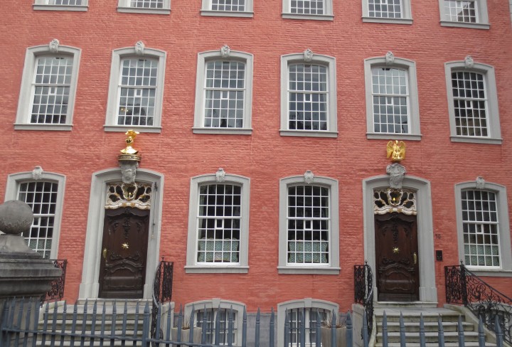 Ansicht eines roten Hauses mit goldenen Hauszeichen über den beiden Eingangstüren