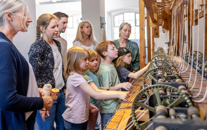 Museumsgästeführerin führt Kindern und Erwachsenen eine Spinnmaschine vor 