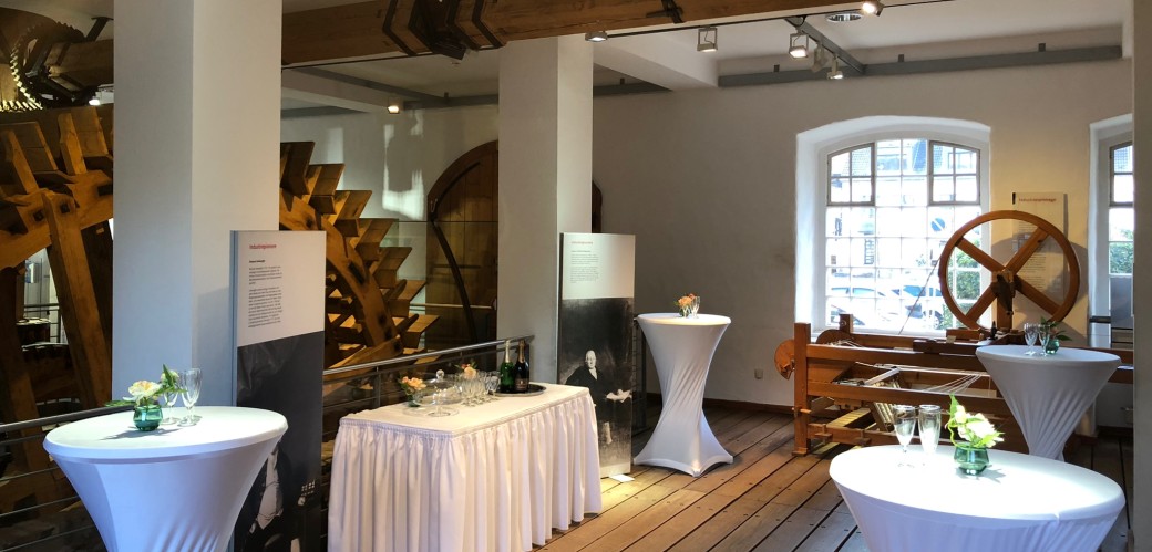 White standing tables stand in front of a wooden water wheel