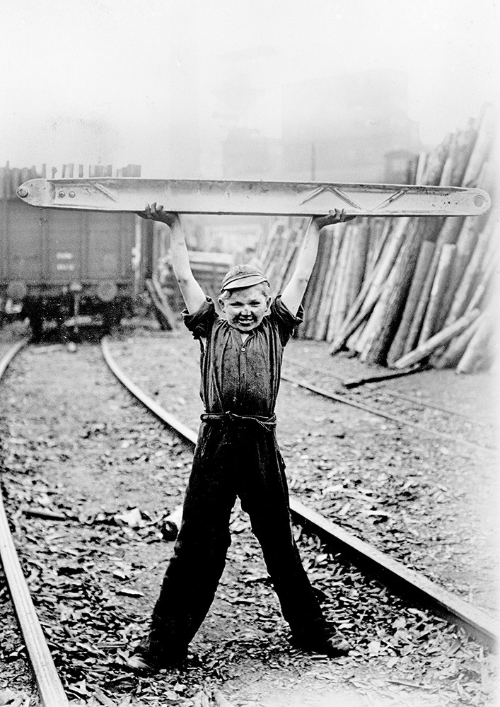 Historisches Schwarzweiß-Foto eines Jungen, der ein großes Bauteil aus Leichtmetall hochhebt