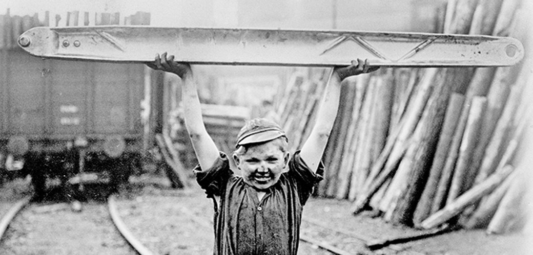 Historisches Schwarzweiß-Foto eines Jungen, der ein großes Bauteil aus Leichtmetall hochhebt