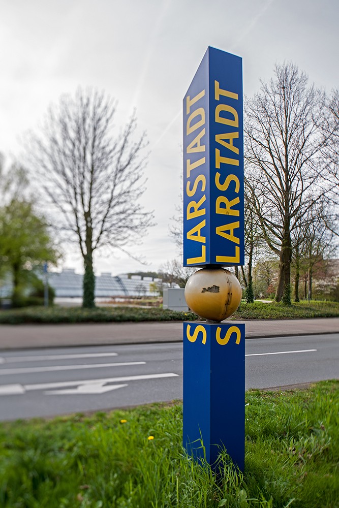 Blaue Stele mit der Aufschrift „Solarstadt“ an einer Straße