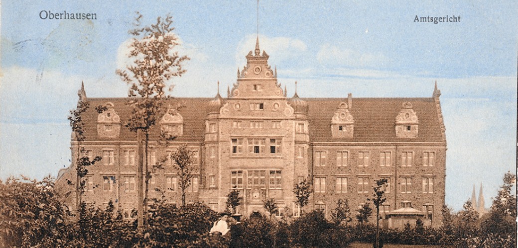 Vorderseite einer Postkarte zeigt ein großes Gebäude, einen Park und zwei spazierende Damen