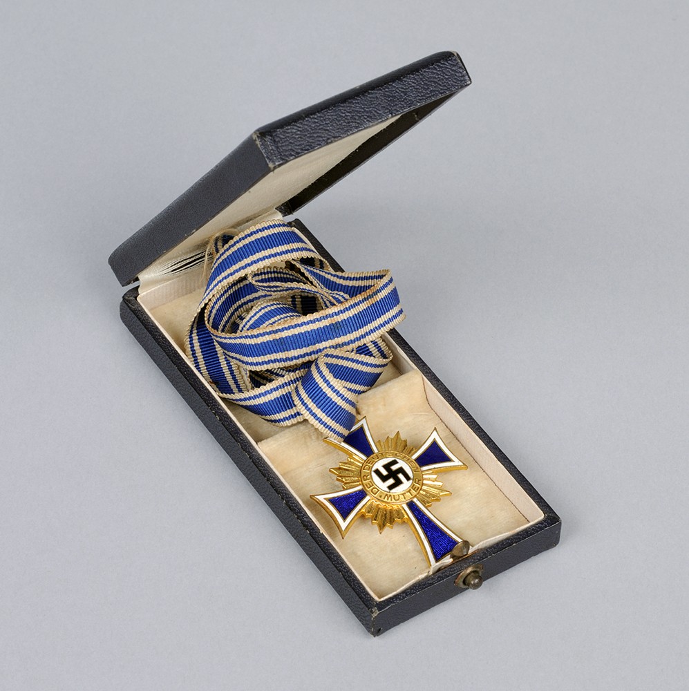 Goldenes Mutterkreuz an blau-weißem Band in einer Schmuckschatulle 