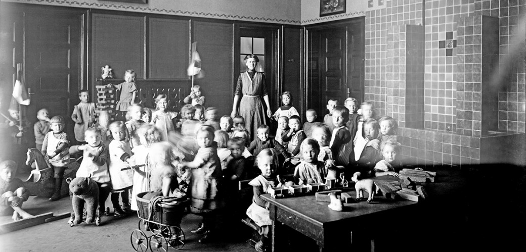 Gruppenfoto der Kleinkinderschule mit Aufseherin im Hintergrund