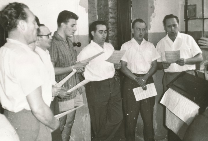 Schwarz-Weiß Foto mit singenden Männern die ein Notenblatt in der Hand haben