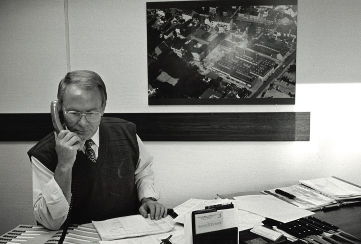 Schwarz-Weiß Foto von einem Mann der an einem Schreibtisch sitzt und telefoniert