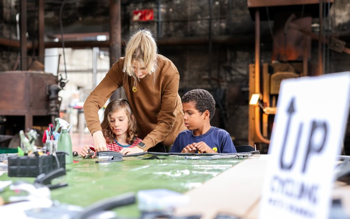 Junge und Mädchen mit einer Museumsmitarbeiterin an einem Basteltisch