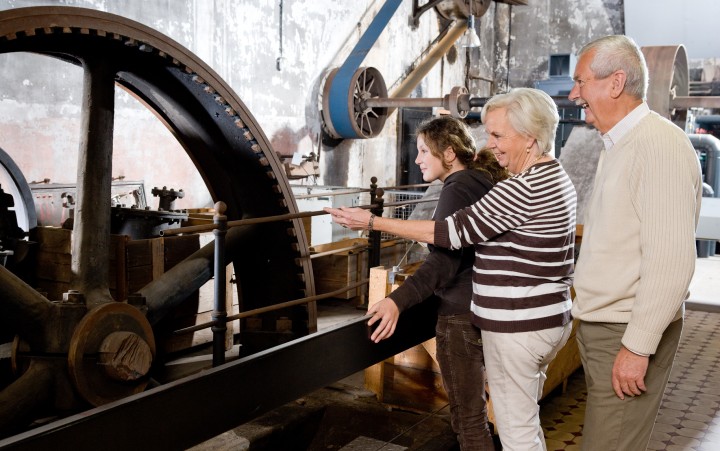 Man and woman with a girl in front of a large flywheel