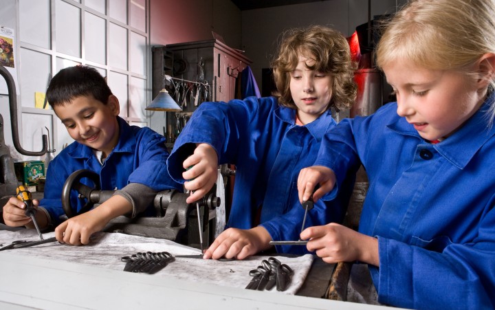 Zwei Jungen und ein Mädchen in Blaumännern bei handwerklicher museumspädagogischer Aktion