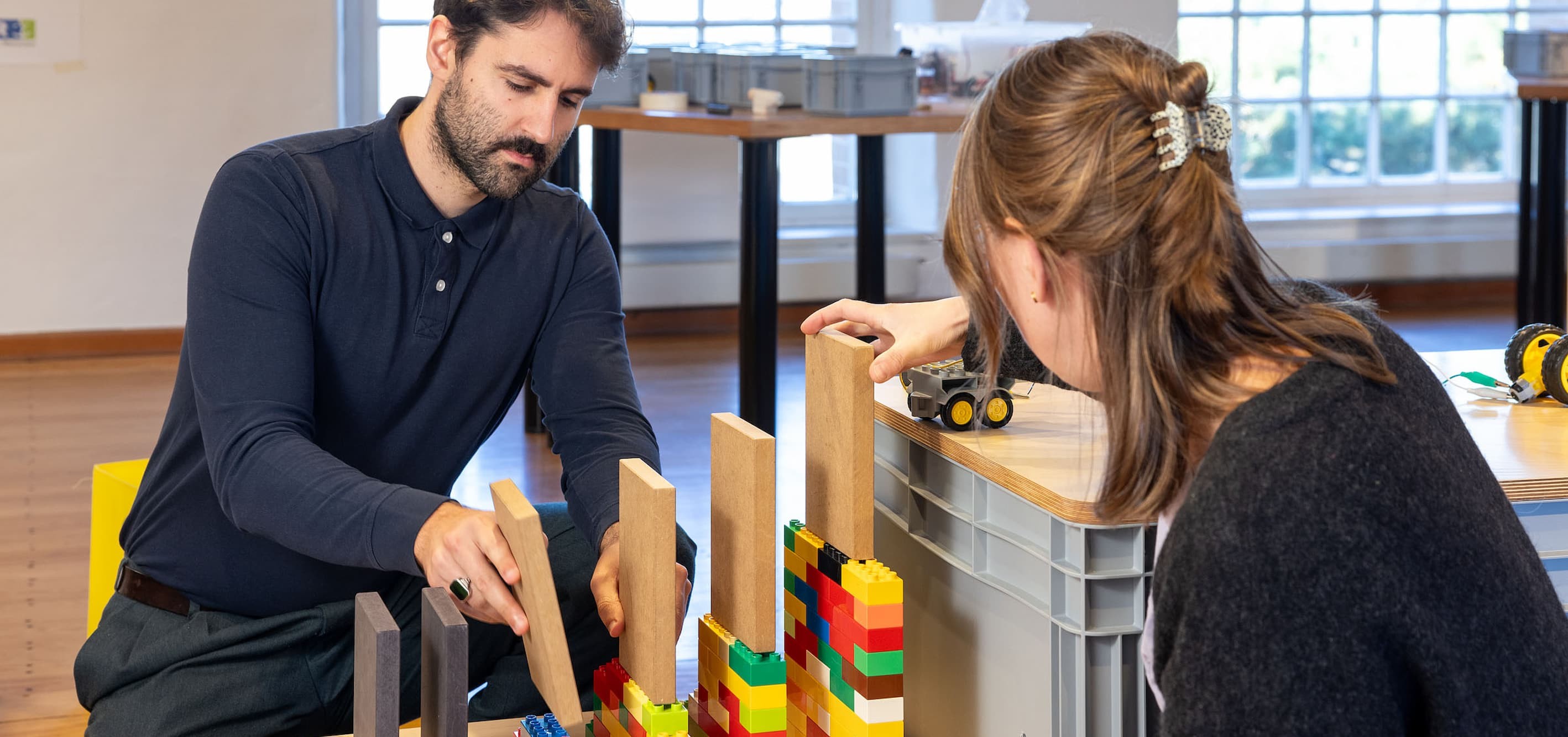 2 Personen bauen große Dominosteine aus Holz auf eine Unterkonstruktion aus Lego