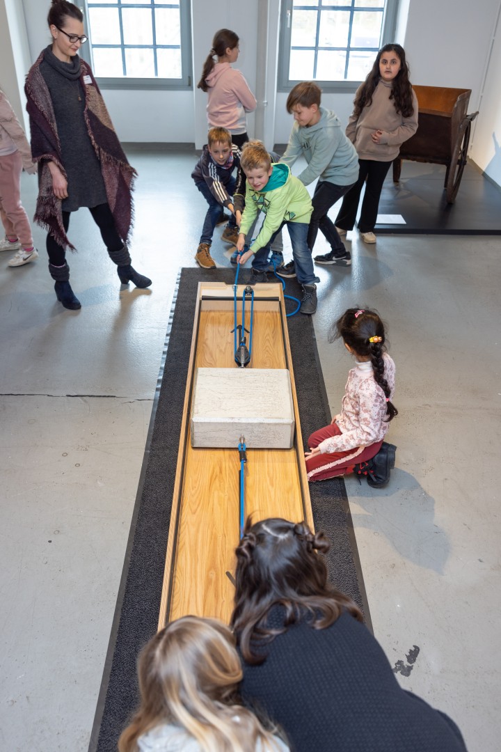 Mädchen und Jungen ziehen an einem Betonklotz in der Ausstellung