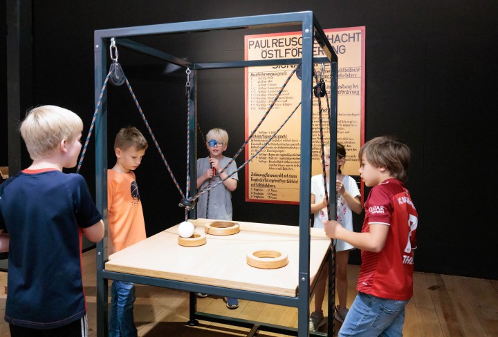Mädchen und Jungen stehen rund um ein Spiel in der Ausstellung