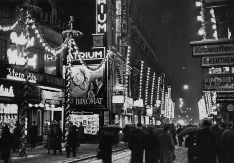 Historisches Schwarzweiß-Foto von einer beleuchteten Einkaufsstraße bei Nacht