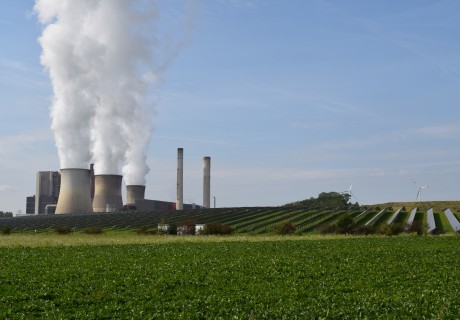 Links Braunkohlekraftwerk mit dampfenden Schornsteinen, rechts Windräder und Solarpanel