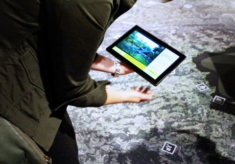 Skizze eines Tablets, das von zwei Händen gehalten wird, im Hintergrund eine Landkarte