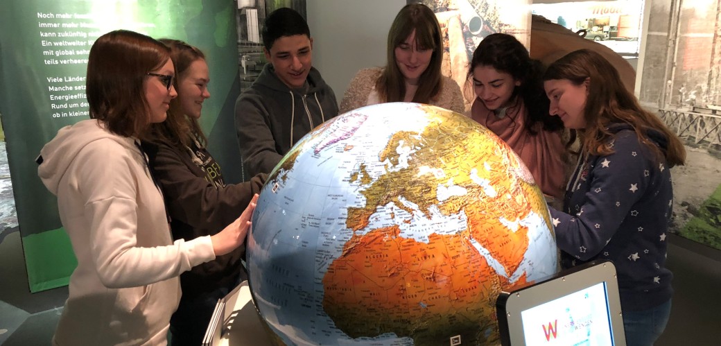 Jugendliche Mädchen und Jungen betrachten einen großen Globus in einer Ausstellung