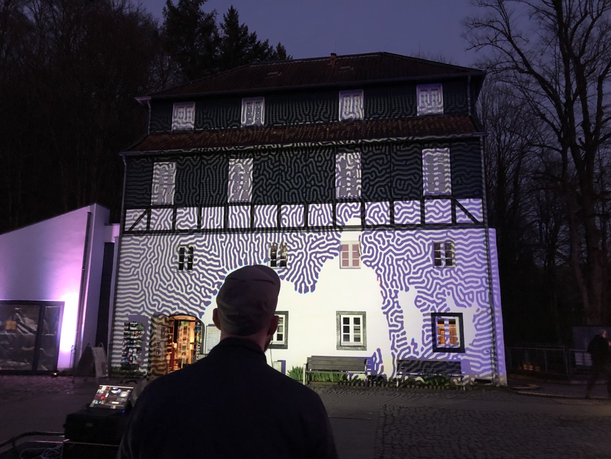 Projektion abstarkter violetter Muster auf einer Hausfassade.