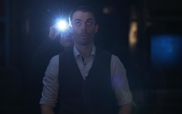 Ein mann in einem dunklen Raum, hinter ihm das Licht einer Taschenlampe
