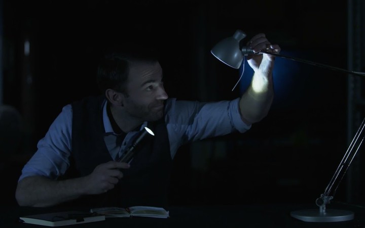 Ein Mann in einem dunklen Raum strahlt mit einer Taschenlampe eine Schreibtischlampe an