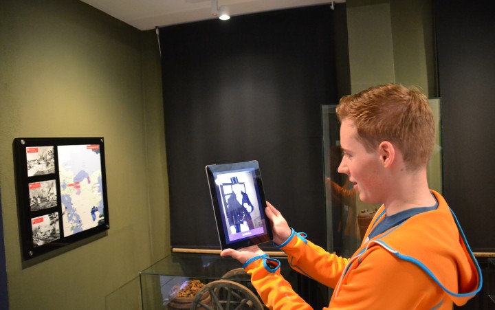 Junger Mann hält ein Tablet auf einen Bildschirm im Museum