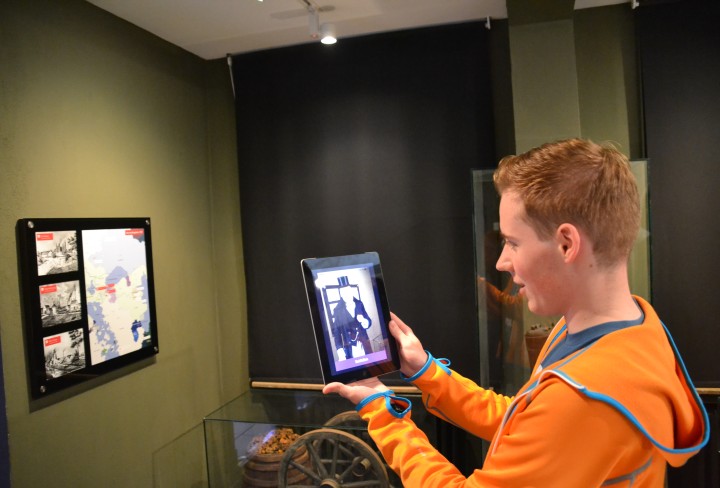 Ein Junge hält ein Tablet in Richtung eines Bildschirms im Museum