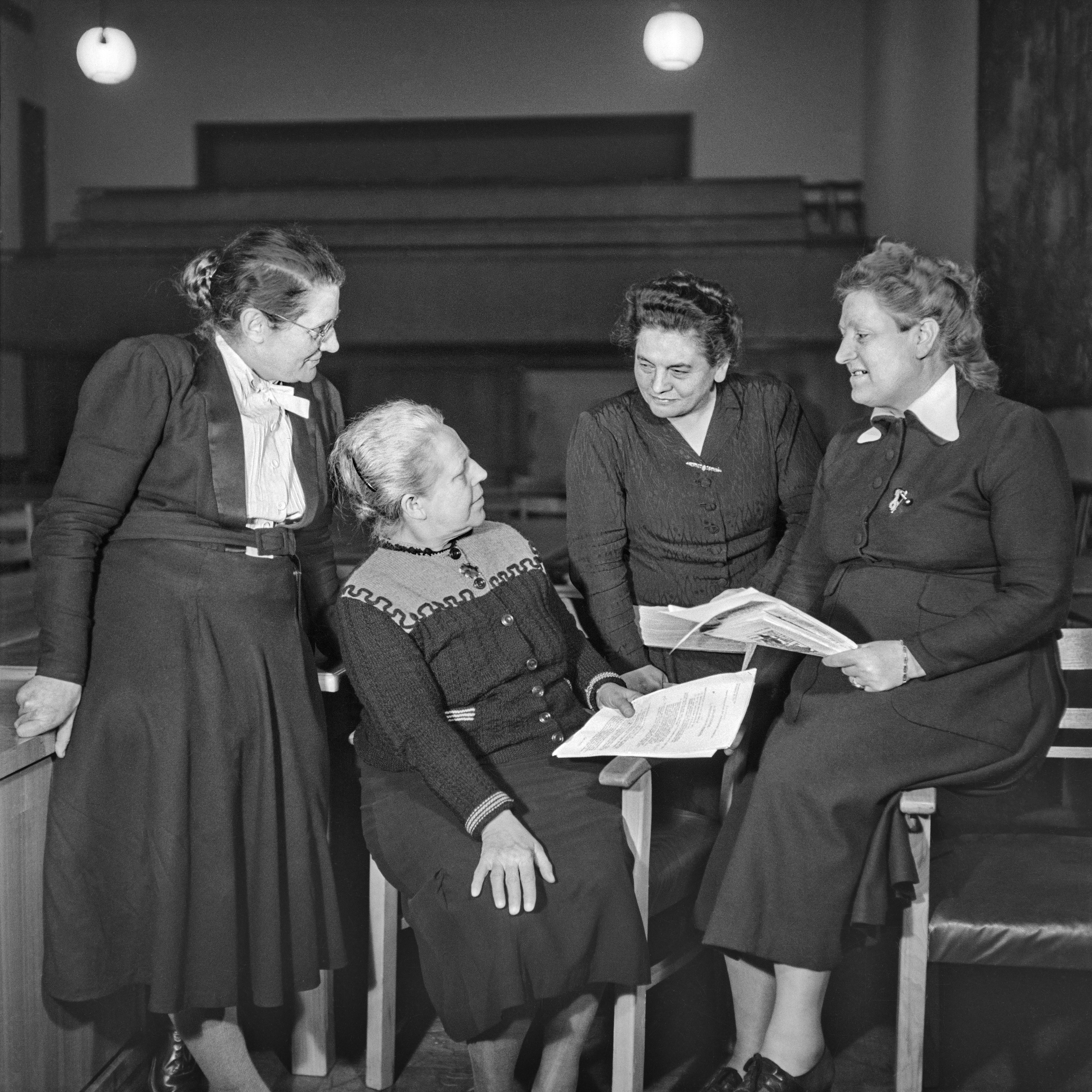 Eine Gruppe von vier Frauen unterhält sich. zwei von ihnen halten Zeitungen oder Dokumente in der Hand.