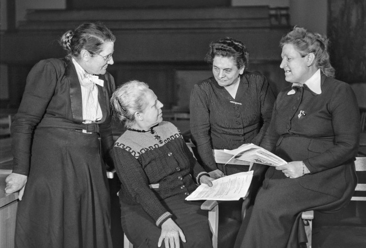 Eine Gruppe von vier Frauen unterhält sich. zwei von ihnen halten Zeitungen oder Dokumente in der Hand.