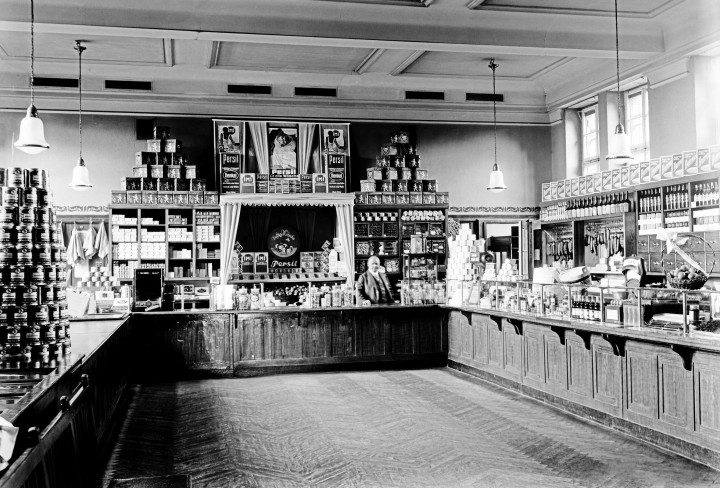 Historisches Schwarz-Weiß Foto zeigt einen alten Verkaufsraum mit Theken und Regalen an den Wänden