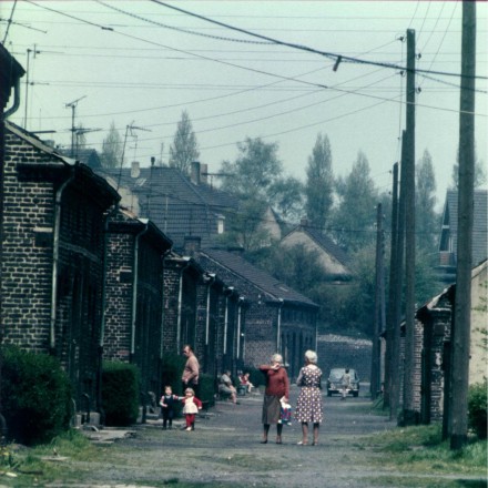Verschiedene Personen halten sich auf einer Straße in Eisenheim auf. Die Straße ist nicht befestigt und an einigen Stellen wächst Unkraut.