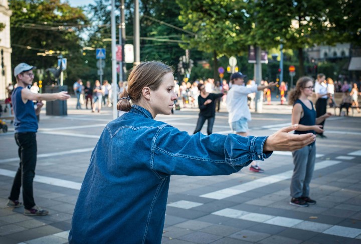 Eine Künstlerin mit Jeansjacke steht mit anderen Frauen in großen Vierecken auf einem Platz