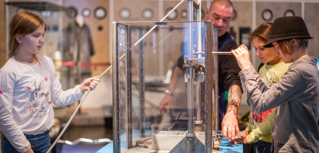 Kinder mit Museumsmitarbeiter an einem Fallhammer-Experiment in der Ausstellung