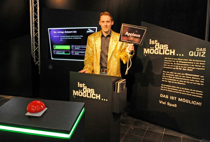 Junge steht als Quizmaster am Pult und hält ein Schild mit der Aufschrift "Applaus" hoch